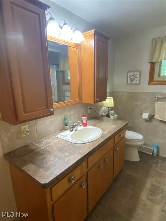 Full bath featuring vanity, tile walls, wainscoting, and stone finish floors
