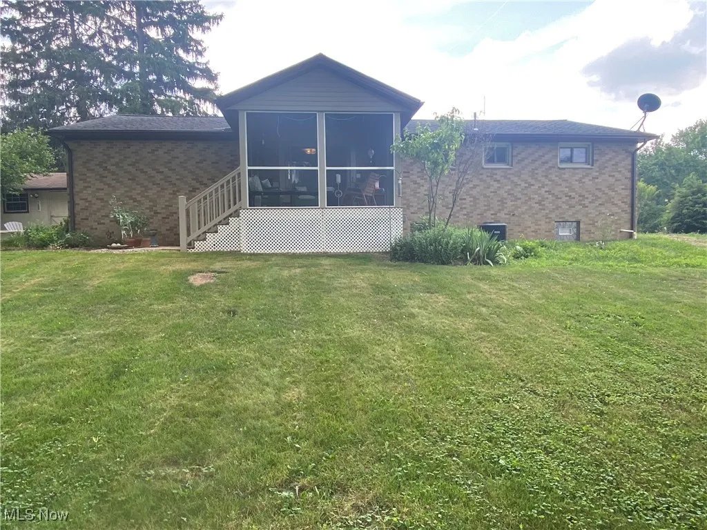 Back of house with brick siding, a sunroom, and a yard