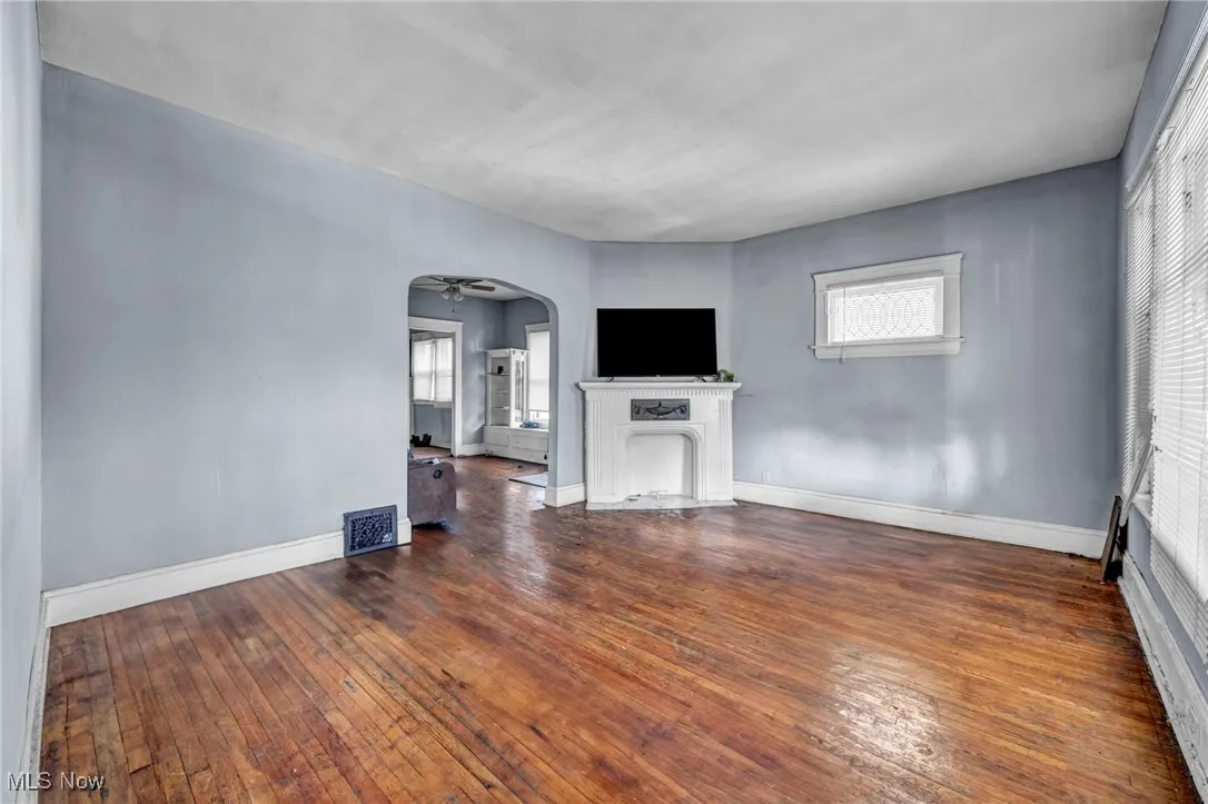 Unfurnished living room with a fireplace with flush hearth, arched walkways, wood-type flooring, and ceiling fan