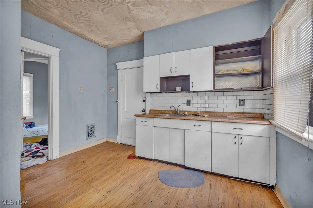 Kitchen with open shelves, light wood finished floors, white cabinets, and backsplash