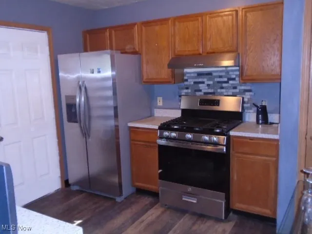 Kitchen with appliances with stainless steel finishes, light countertops, dark wood finished floors, and brown​​‌​​​​‌​​‌‌​‌‌​​​‌‌​‌​‌​‌​​​‌​​ cabinets