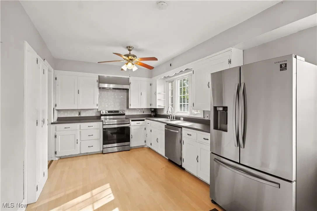 Kitchen featuring stainless steel appliances, dark countertops, white cabinetry, and a ceiling fan