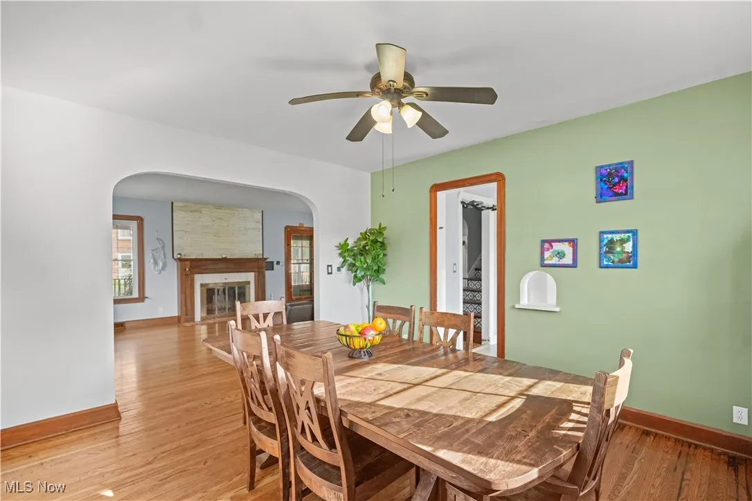 Dining space with arched walkways, ceiling fan, light wood-style flooring, and a fireplace