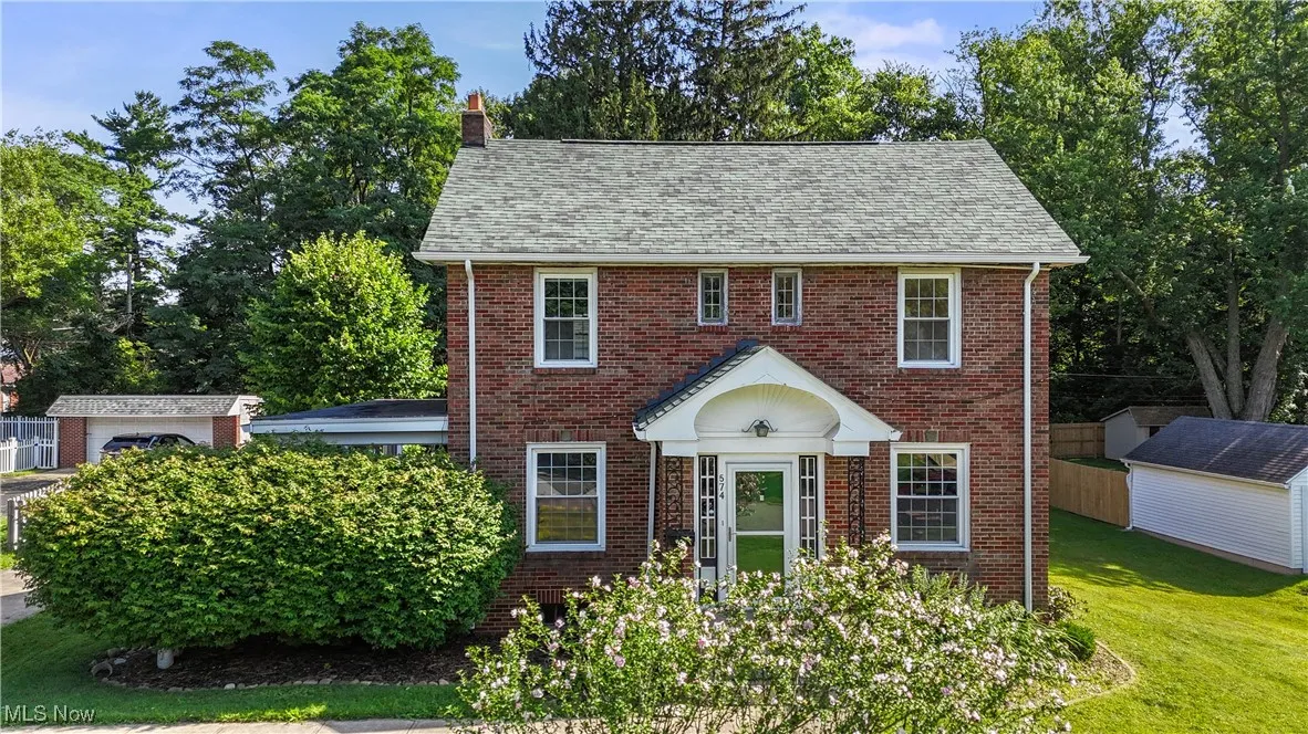 Colonial-style house with a chimney, brick siding, a front lawn, and a shingled roof
