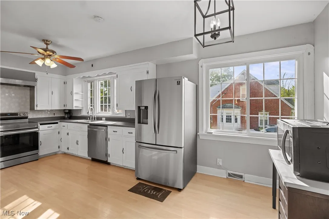 Kitchen featuring stainless steel appliances, light wood-type flooring, wall chimney range hood, and white cabinetry