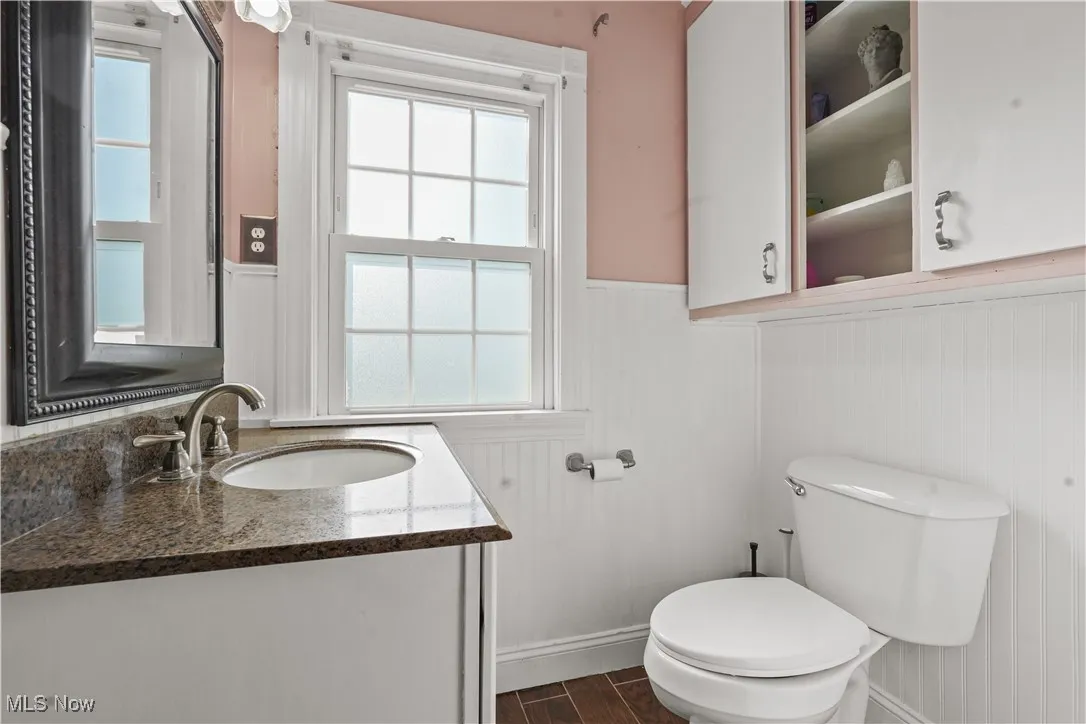 Half bath featuring vanity, a wainscoted wall, healthy amount of natural light, and wood finished floors
