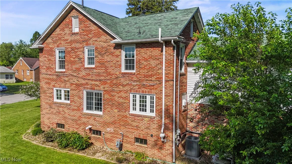 View of side of property featuring a lawn, brick siding, and a shingled roof