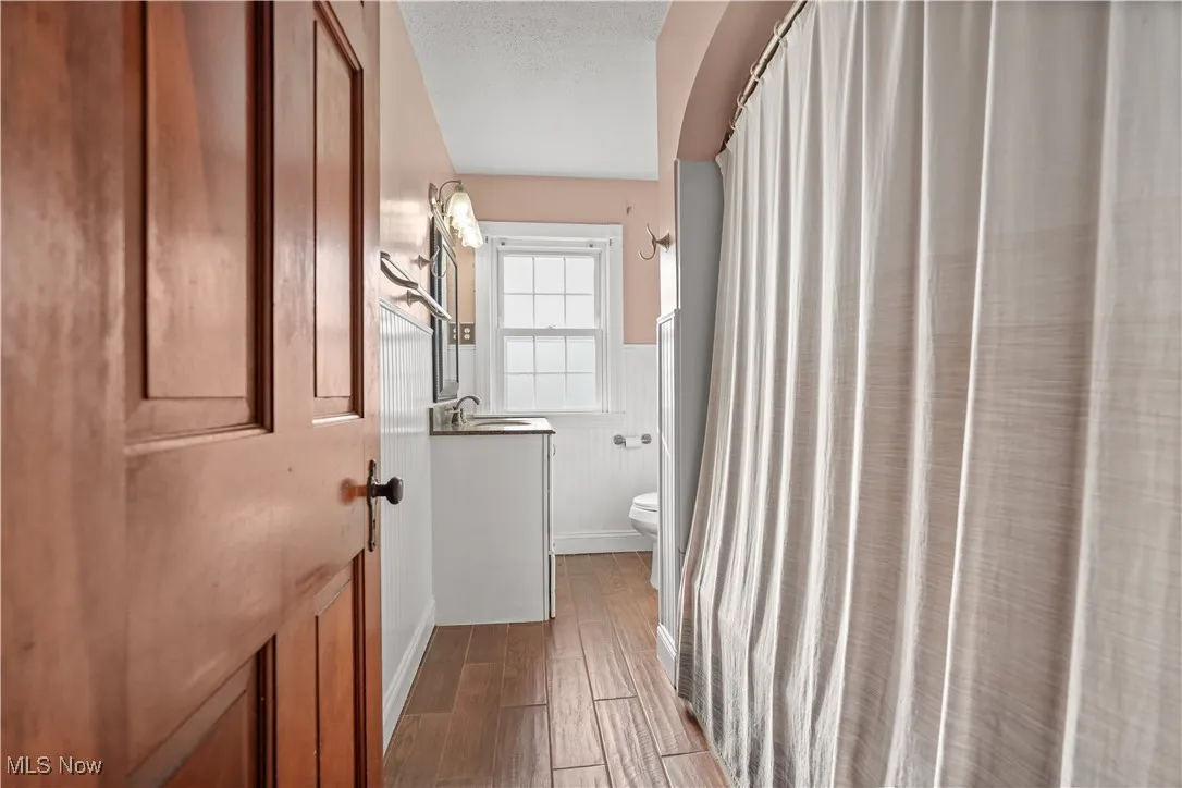 Bathroom with a wainscoted wall, vanity, wood finished floors, and curtained shower