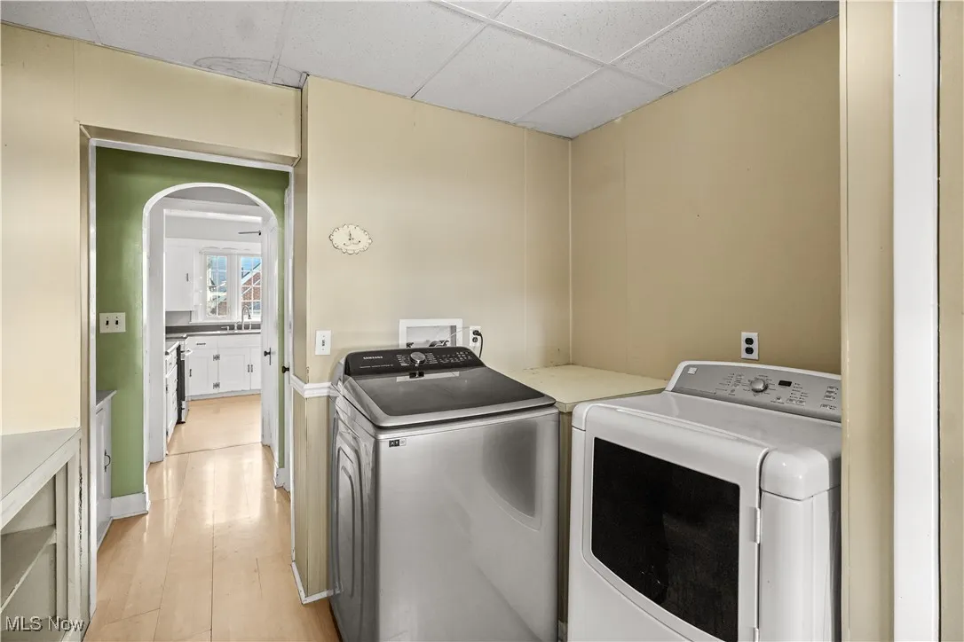 Laundry room featuring washing machine and clothes dryer, light wood-type flooring, and arched walkways