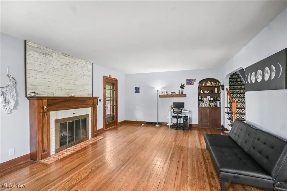 Living room with wood finished floors, built in shelves, a stone fireplace, and an office area