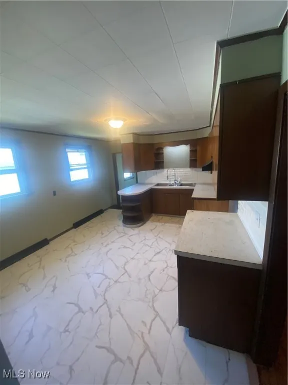 Kitchen featuring light marble finish flooring, light countertops, open shelves, and brown cabinets