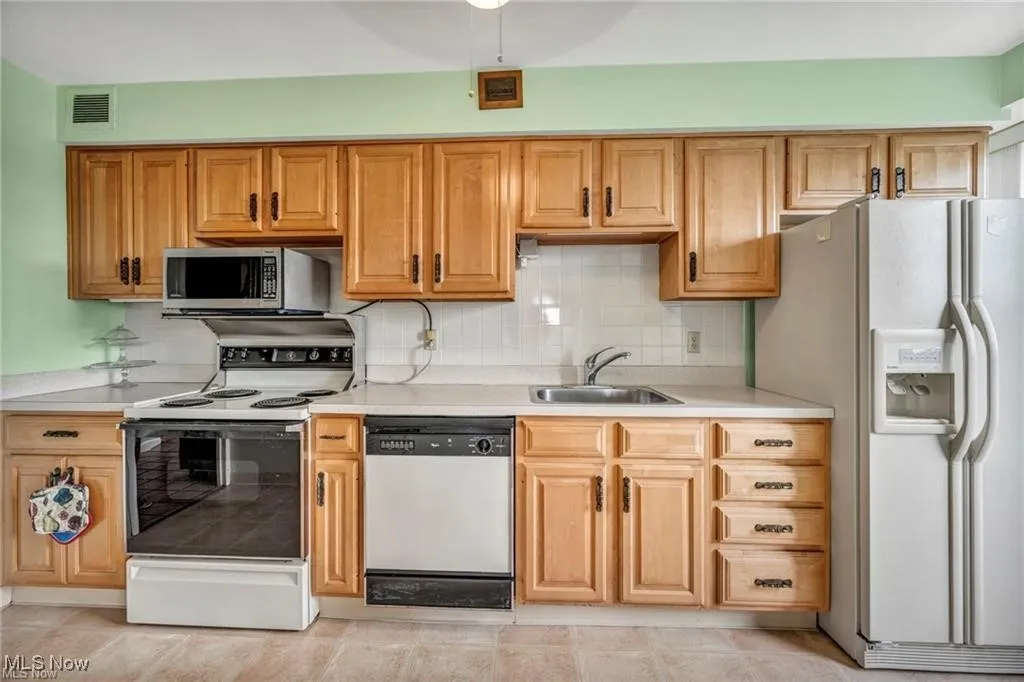 Kitchen featuring electric stove, white fridge with ice dispenser, dishwashing machine, light countertops, and stainless steel microwave