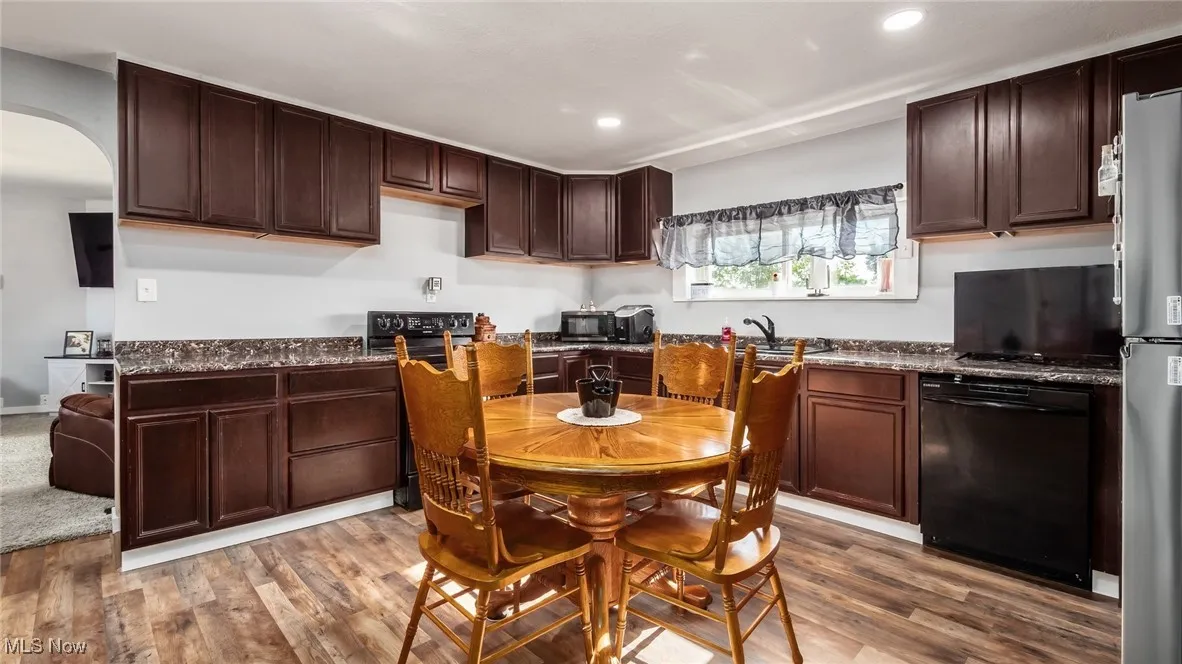 Kitchen featuring black dishwasher, arched walkways, wood finished floors, recessed lighting, and freestanding refrigerator