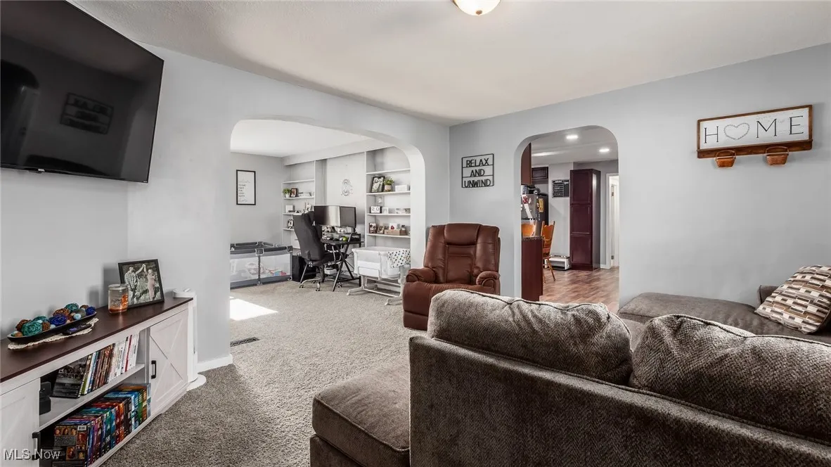 Carpeted living room featuring arched walkways, an office area, and built in shelves