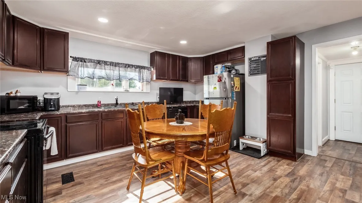 Kitchen with black appliances, light wood-style flooring, dark countertops, recessed lighting, and dark brown cabinetry