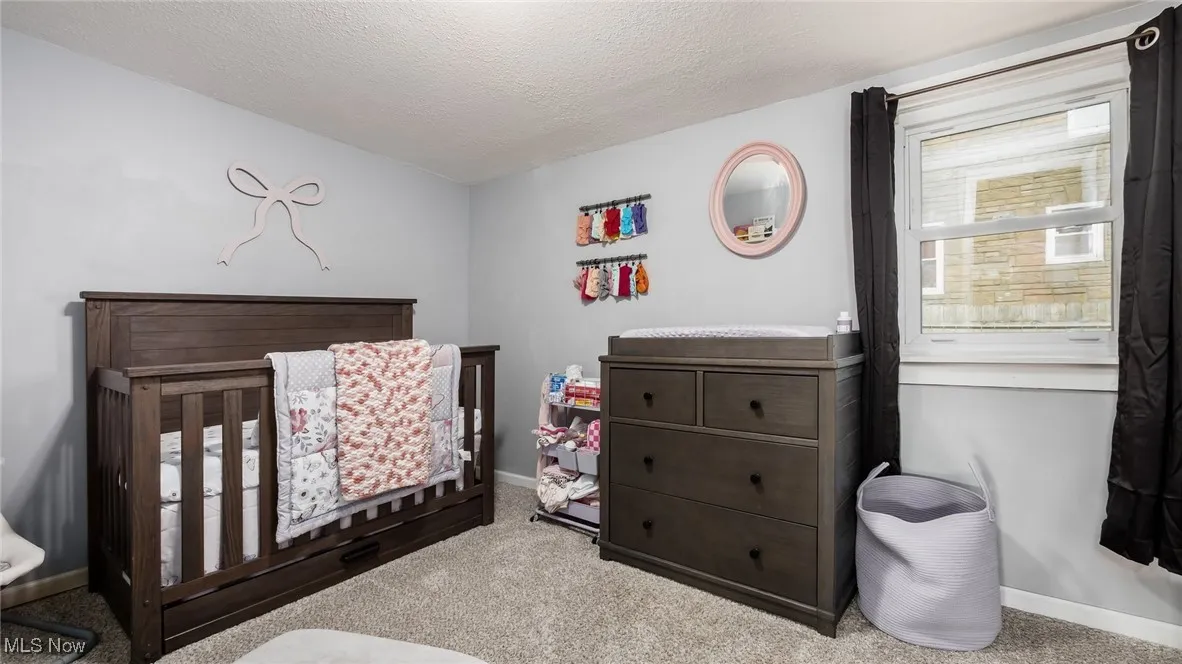 Carpeted bedroom featuring a crib and a textured ceiling