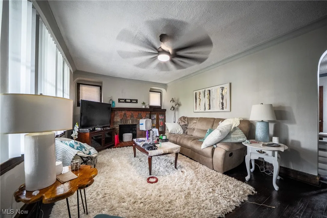 Living area featuring a textured ceiling, plenty of natural light, ornamental molding, wood finished floors, and a brick fireplace