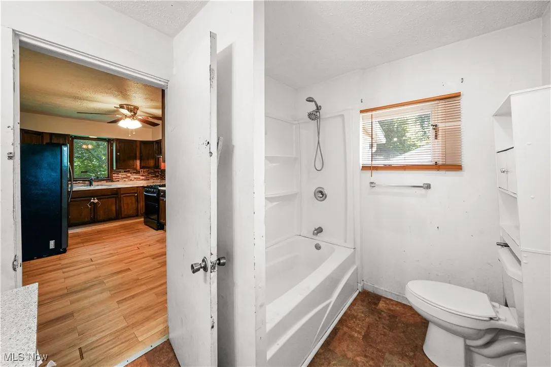 Full bath featuring a textured ceiling, vanity, bathtub / shower combination, a ceiling fan, and backsplash