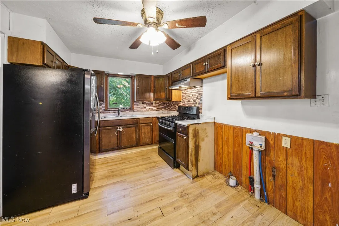 Kitchen with black appliances, ceiling fan, wainscoting, a textured ceiling, and light wood-style flooring