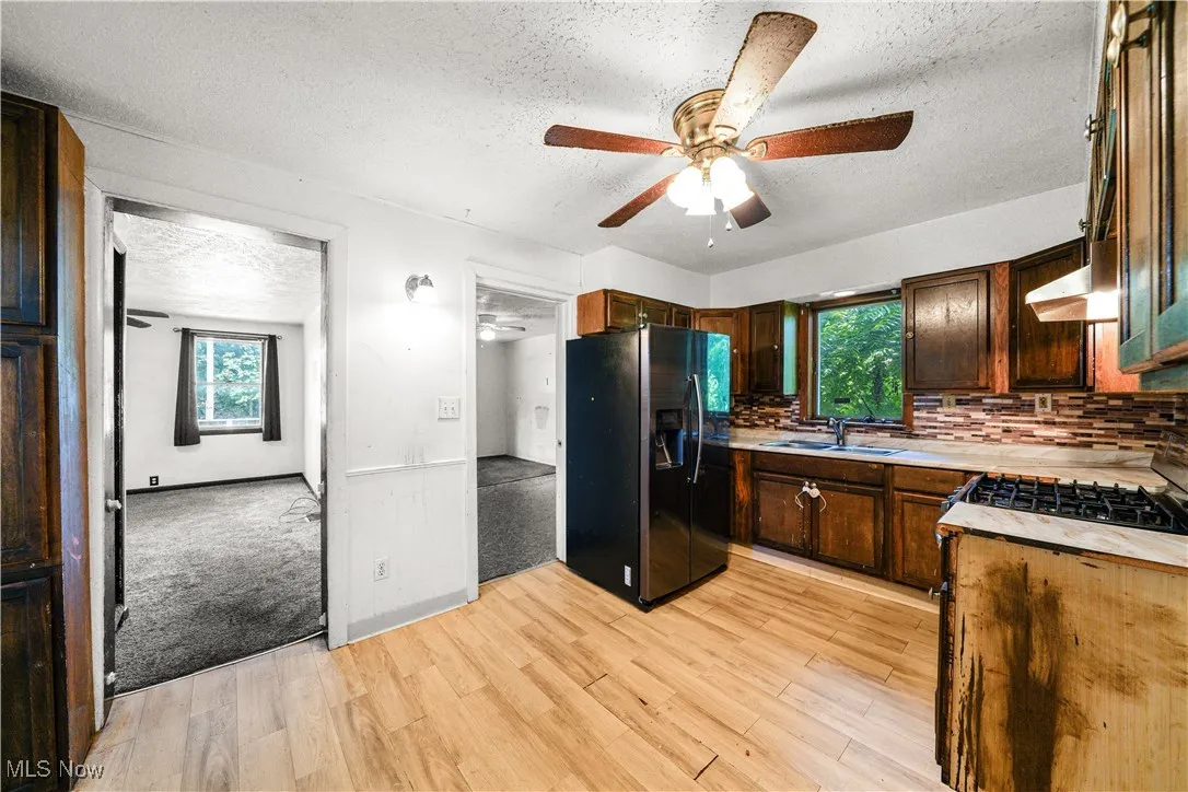 Kitchen with a textured ceiling, a ceiling fan, black refrigerator with ice dispenser, backsplash, and light wood-style flooring