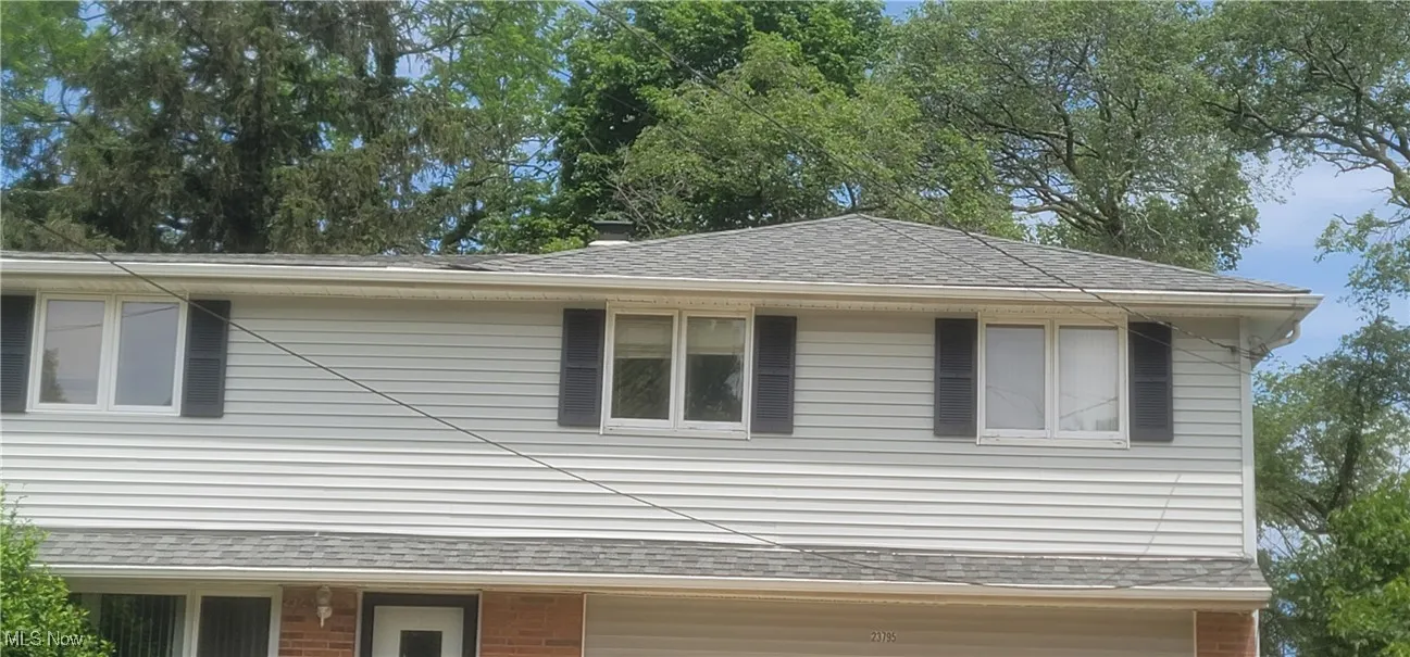 View of property exterior featuring roof with shingles and brick siding