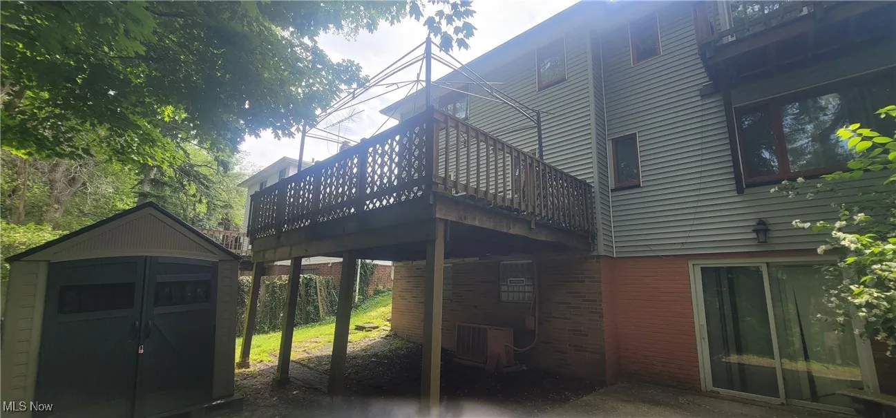 Back of property featuring a storage shed, brick siding, and a wooden deck