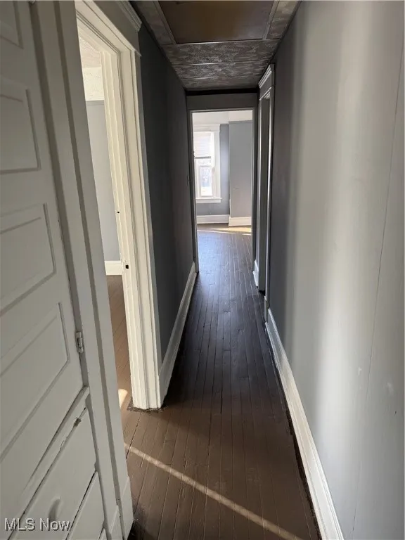Hallway with dark wood-type flooring and baseboards
