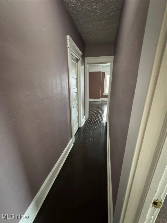 Corridor featuring a textured ceiling and dark wood-type flooring