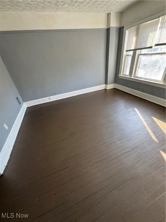 Empty room with dark wood-type flooring and a textured ceiling