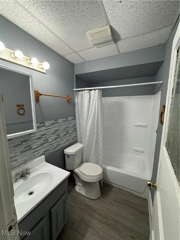 Full bath with a paneled ceiling, vanity, wood finished floors, shower / bath combo, and wainscoting