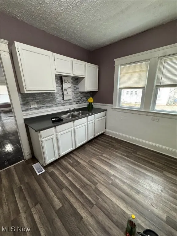 Kitchen featuring white cabinetry, dark wood finished floors, a textured ceiling, decorative backsplash, and dark countertops