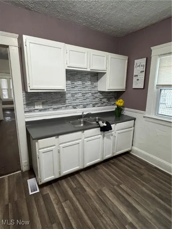 Kitchen featuring white cabinets, a textured ceiling, dark wood finished floors, and decorative backsplash