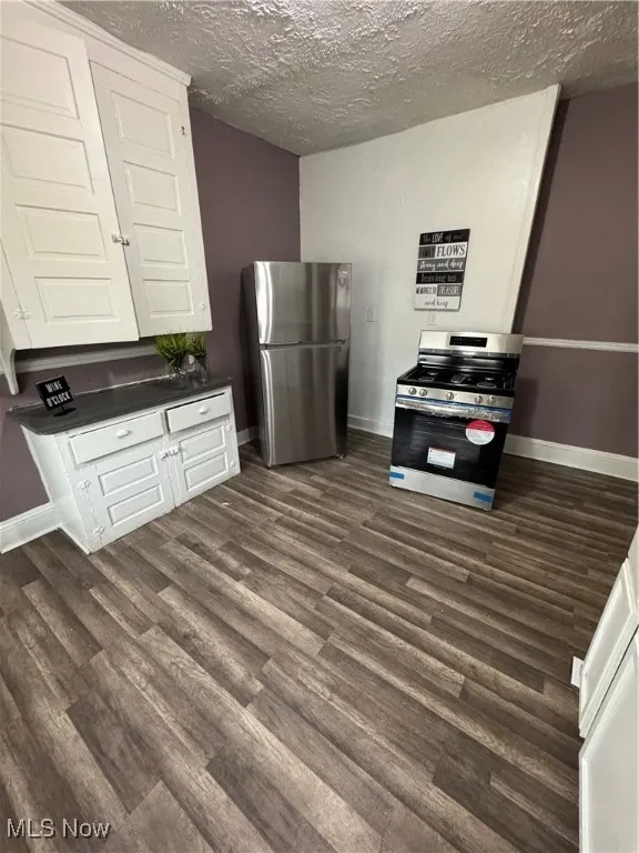 Kitchen with range, fridge, dark wood-type flooring, dark countertops, and a textured ceiling
