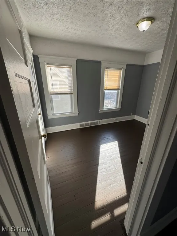 Empty room featuring a textured ceiling and dark wood finished floors