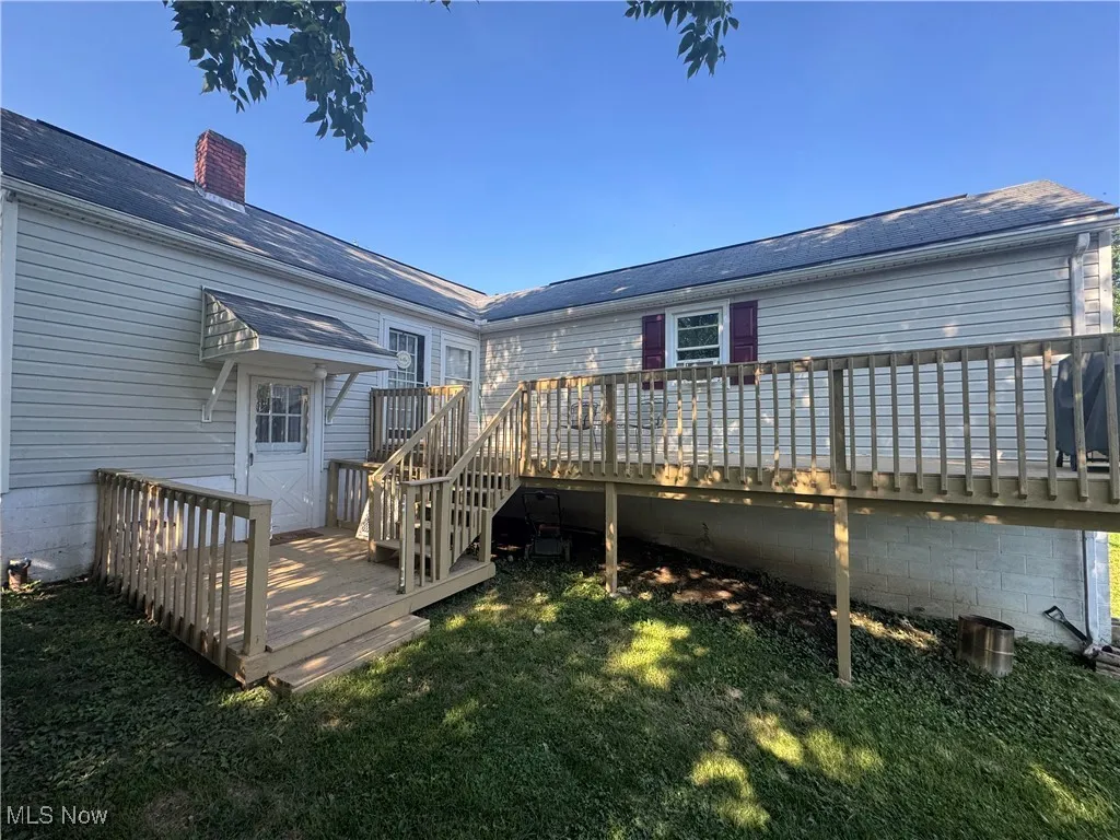 Rear view of house with a wooden deck, a chimney, and a lawn