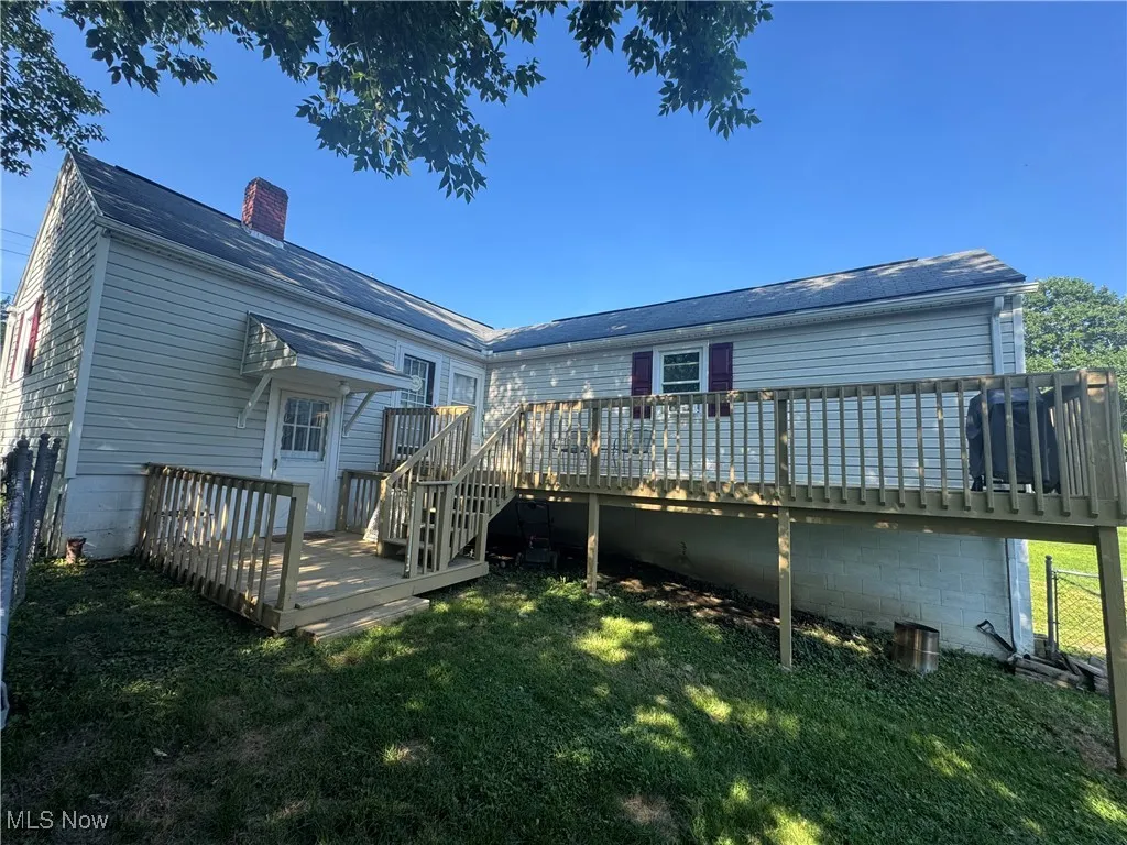 Rear view of property with a chimney, a deck, and a lawn