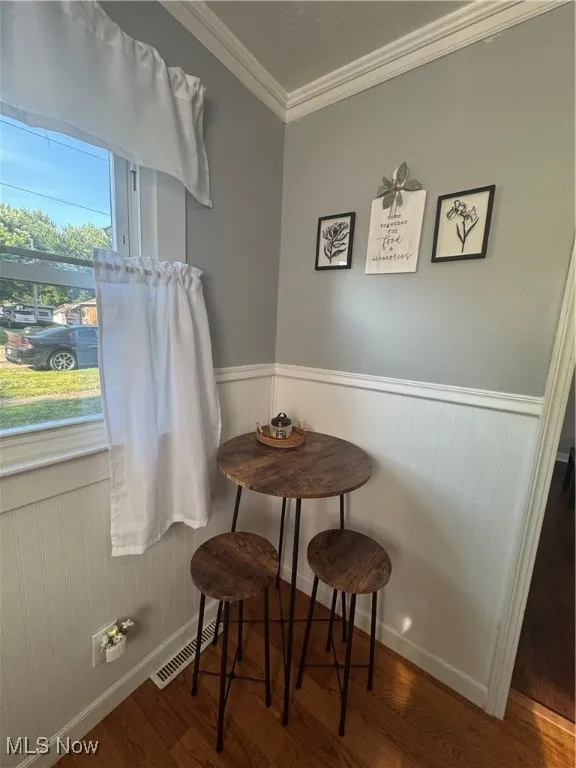 Dining area featuring ornamental molding, wood finished floors, and a wainscoted wall