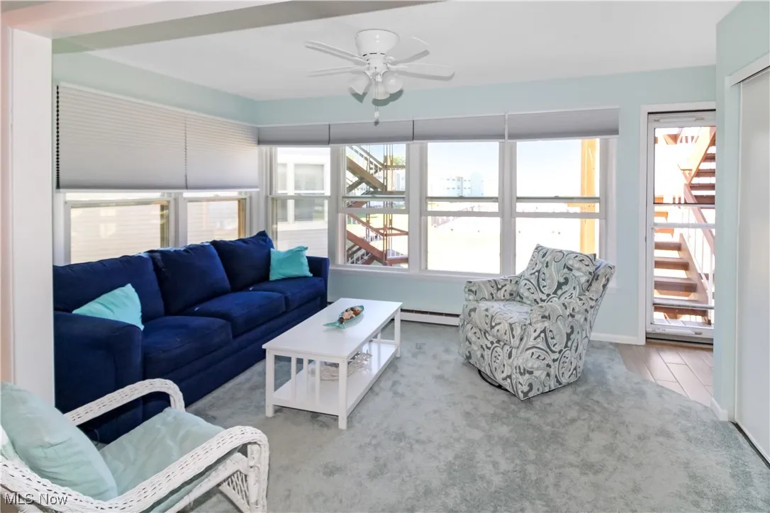 Living area with a ceiling fan, baseboard heating, and stairway