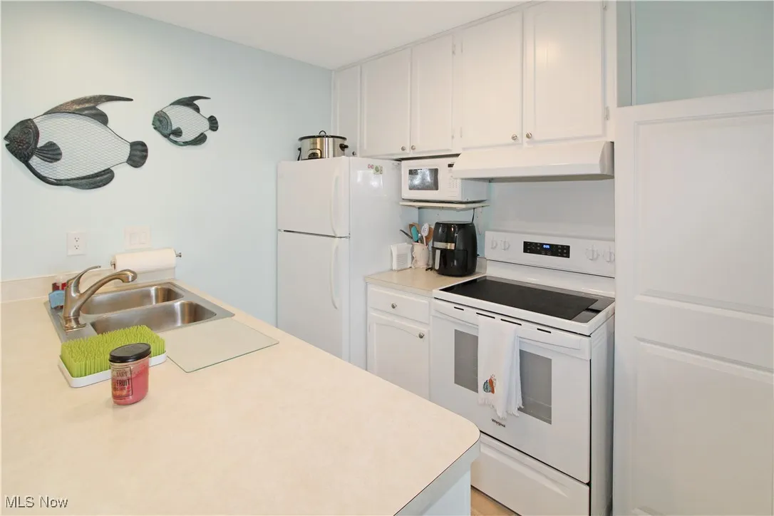 Kitchen featuring white appliances, under cabinet range hood, white cabinetry, and light countertops