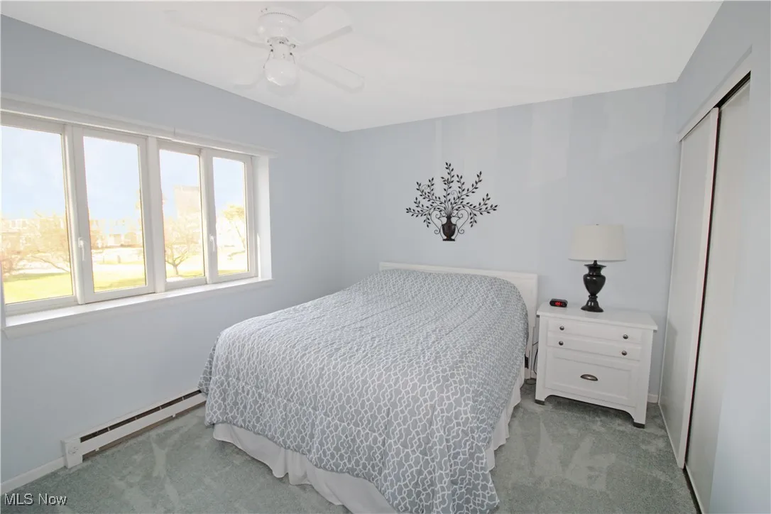 Bedroom with light carpet, a baseboard heating unit, a closet, and a ceiling fan