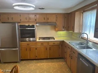 Kitchen featuring stainless steel appliances, light countertops, brown cabinetry, and under cabinet range hood