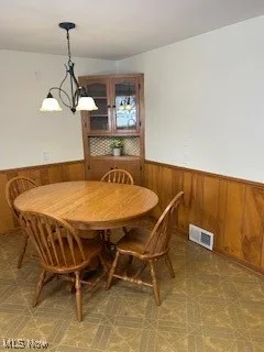 Dining space featuring a wainscoted wall, wooden walls, light floors, and a chandelier
