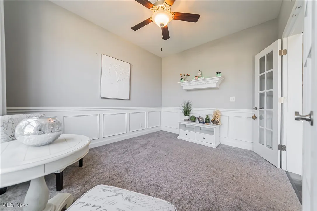 Living area with carpet floors, a wainscoted wall, and a ceiling fan