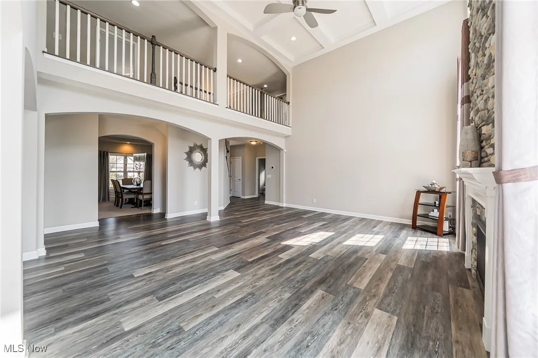 Unfurnished living room with arched walkways, a ceiling fan, a towering ceiling, wood finished floors, and beam ceiling