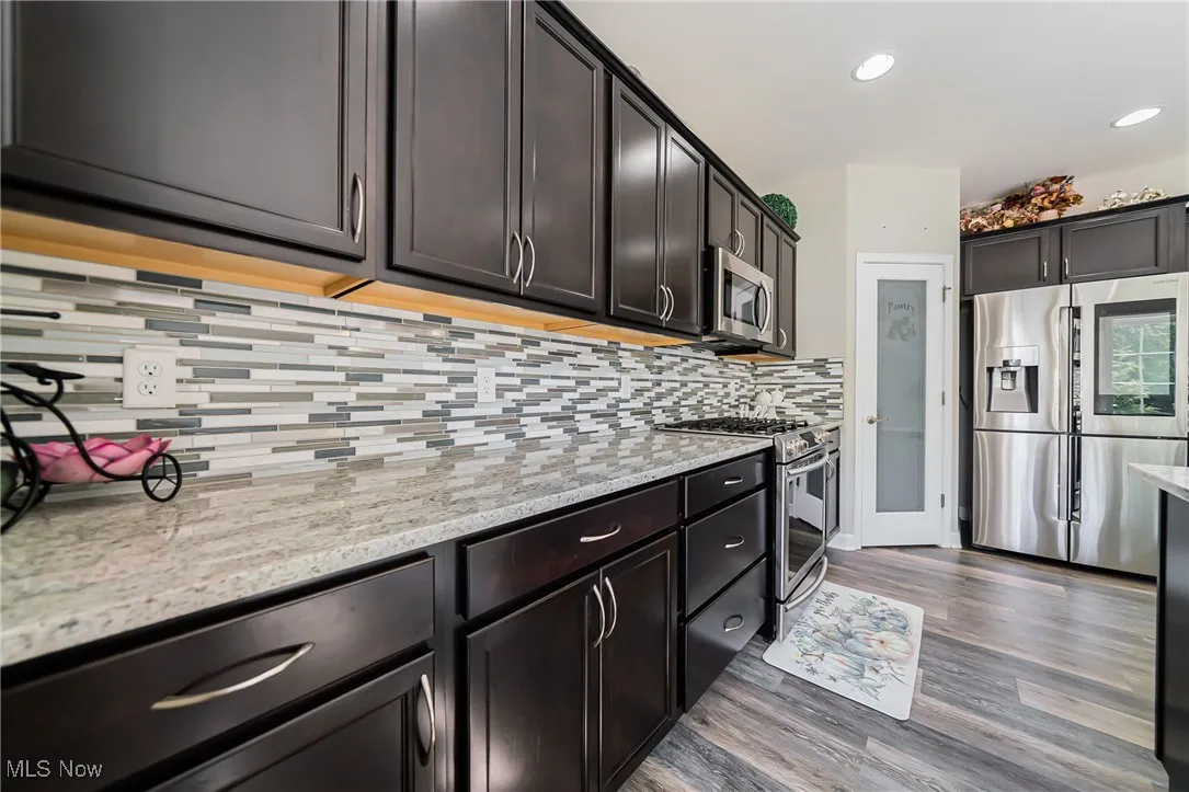 Kitchen featuring stainless steel appliances, dark wood finished floors, tasteful backsplash, light stone countertops, and dark brown cabinets