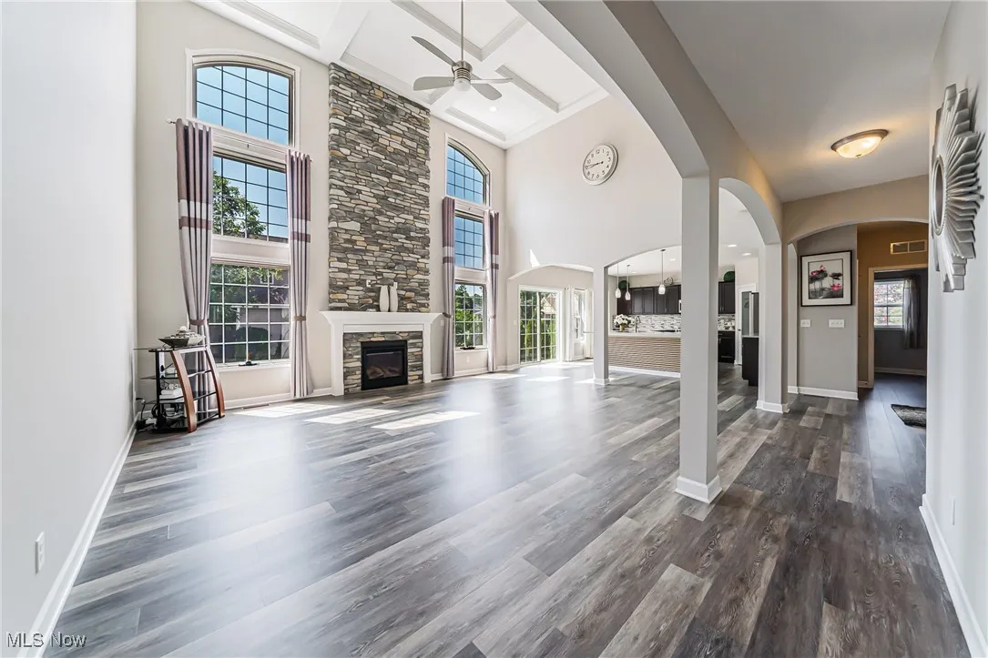 Unfurnished living room with ceiling fan, a high ceiling, dark wood finished floors, a stone fireplace, and beam ceiling