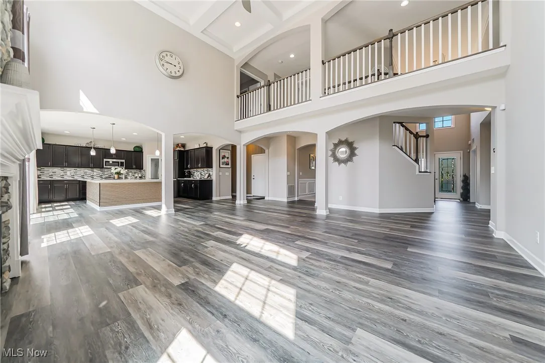 Unfurnished living room featuring a towering ceiling, wood finished floors, stairs, beamed ceiling, and arched walkways