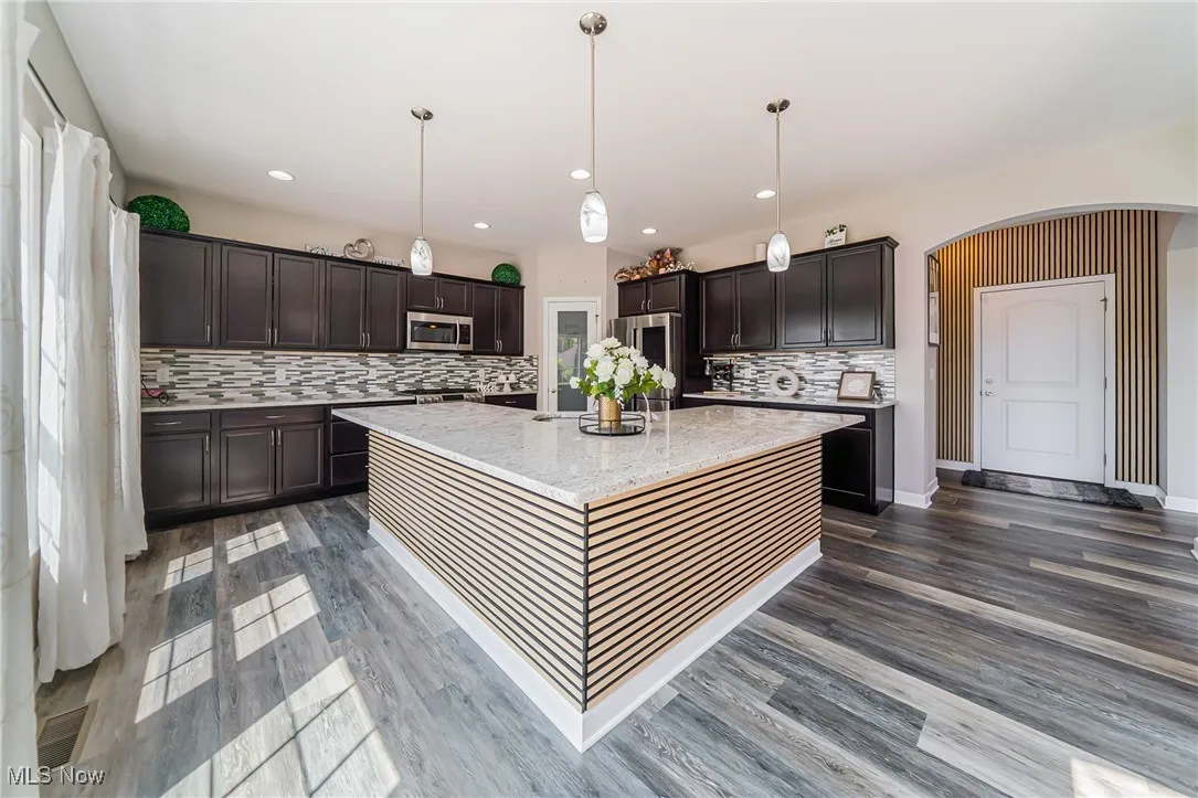Kitchen with dark brown cabinets, tasteful backsplash, arched walkways, stainless steel appliances, and dark wood-type flooring
