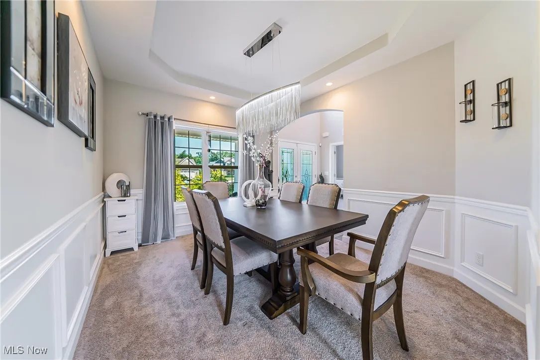 Dining room featuring light colored carpet, arched walkways, a decorative wall, a raised ceiling, and a wainscoted wall