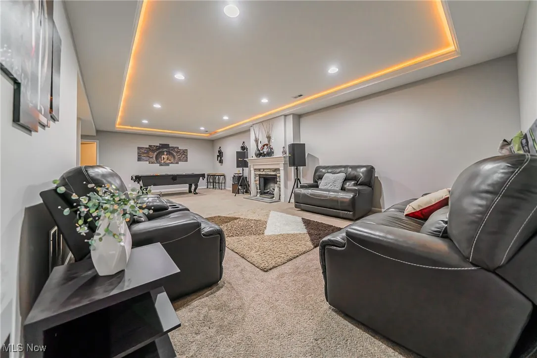 Carpeted living area with a tray ceiling, recessed lighting, and a fireplace